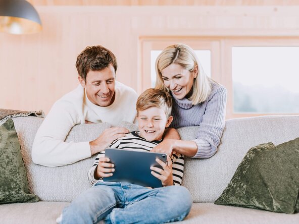 Familie sitzt in Wohnzimmer auf Sofa und spielt mit Tablet
